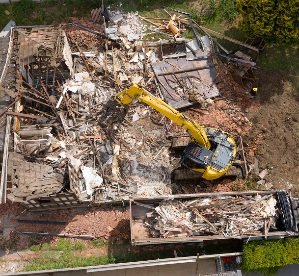 Excavatrice jaune démolissant un bâtiment en ruines, entourée de gravats et de débris sur un chantier.